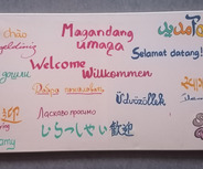 Das Bild zeigt verschiedene Begrüßungen in mehreren Sprachen. 