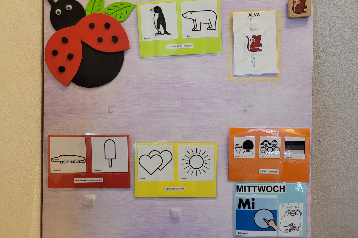 Das Bild zeigt ein buntes Wandbrett mit verschiedenen Symbolen und Illustrationen. Es enthält einem Marienkäfer, Karten mit einem Pinguin, einem Eisbären, einem Krokodil, einem Eis und zwei Herzen. Ein Abschnitt ist für den Mittwoch (Mi) gekennzeichnet, und es gibt eine freundliche Aufforderung zum Abschied.
