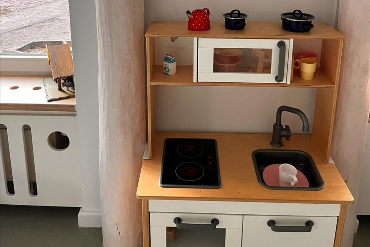 Das Bild zeigt eine kleine Spielküche mit einem Herd, einem Waschbecken und einer Mikrowelle. 