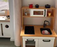 Das Bild zeigt eine kleine Spielküche mit einem Herd, einem Waschbecken und einer Mikrowelle. 