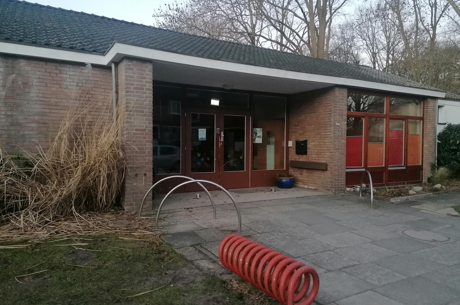 Eingang zu einem modernen, einstöckigen Gebäude mit Backsteinfassade und großen Fenstern.