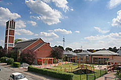 Eine Ansicht eines Gebäudes mit einer modernen Architektur. Im Vordergrund ist ein Spielplatz mit Spielgeräten, umgeben von grünen Flächen.