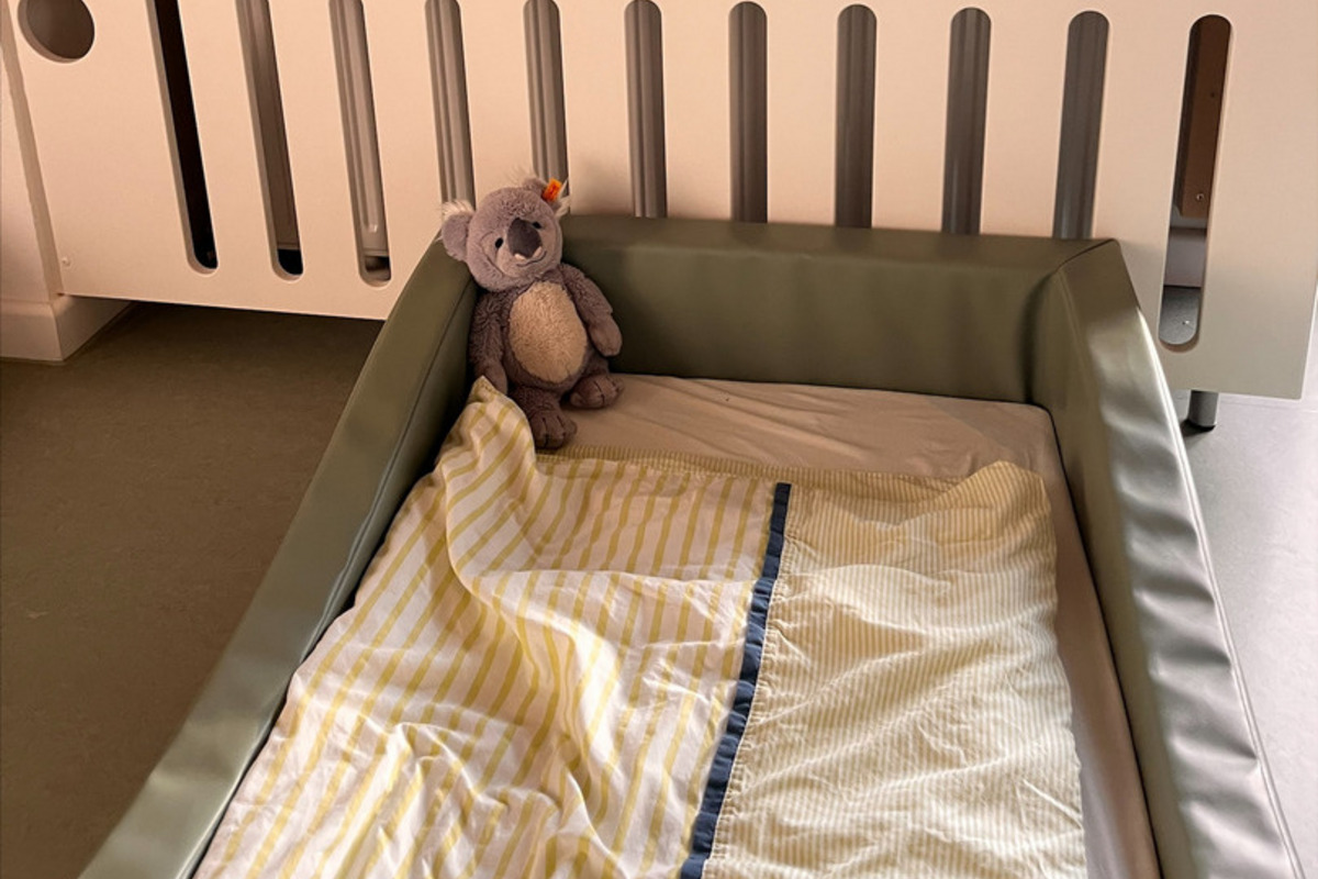 Ein Kinderbett mit einer grünen Umrandung steht im Vordergrund. 