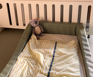 Ein Kinderbett mit einer grünen Umrandung steht im Vordergrund. 