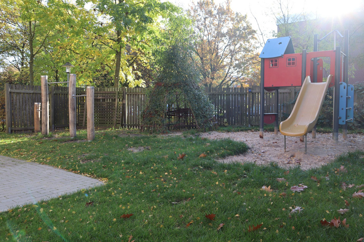 Ein Spielplatz im Freien mit einer Rutsche, einem Spielhaus in leuchtenden Farben und einigen Holzpfosten.