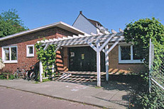 Ein einstöckiges Gebäude mit roter Backsteinfassade und einem weißen, schattenspendenden Vordach. 