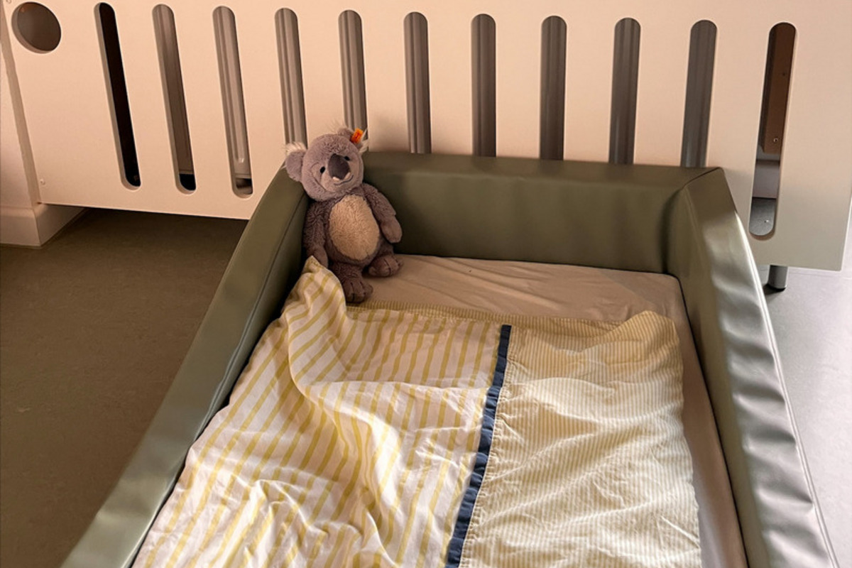 Ein Kinderbett mit einer grünen Umrandung steht im Vordergrund. 