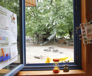 Blick aus einem Fenster auf einen Kindergartenbereich mit Spielgeräten. 