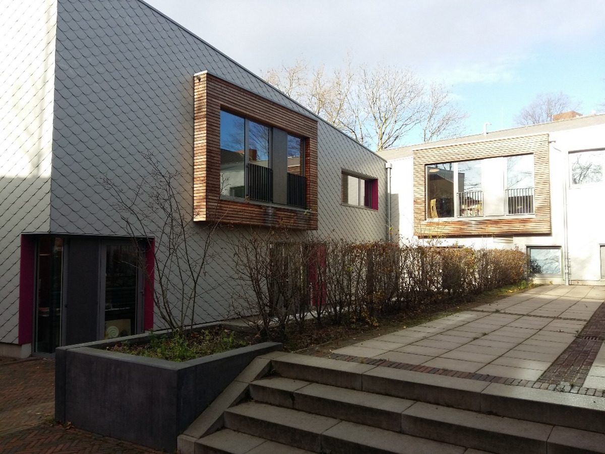 Ein modernes Gebäude mit einer schlichten, grauen Fassade und großen Fenstern, die mit Holzrahmen umrandet sind.