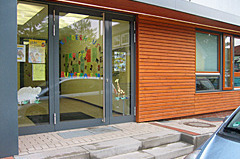 Der Eingang eines Kindergartens mit großen Glastüren und bunten Zeichnungen im Fenster. 