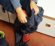 Ein Kind zieht sich eine dunkle Hose an. 