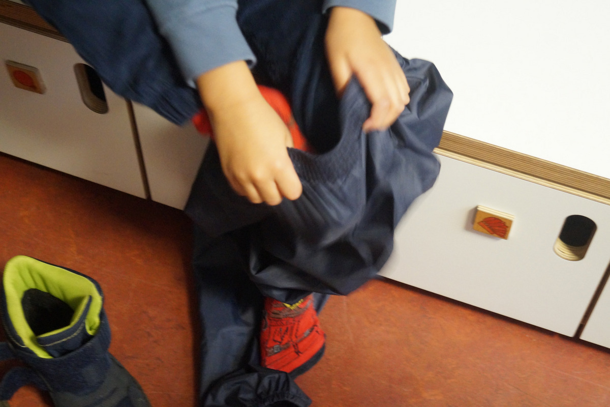 Ein Kind zieht sich eine dunkle Hose an. 