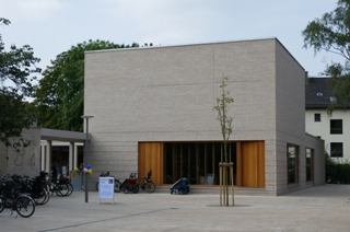 Ein modernes, rechteckiges Gebäude mit hellem Mauerwerk und großen, verglasten Fenstern. Vor dem Gebäude stehen Fahrräder abgestellt.