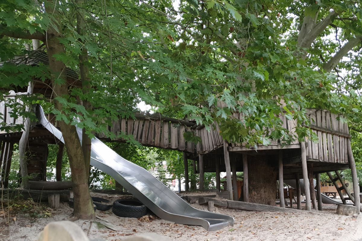 Auf dem Bild ist ein Spielplatz zu sehen, der aus einem Holzspielhaus mit einer Rutsche besteht. 
