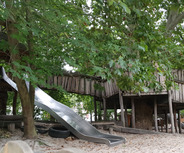 Auf dem Bild ist ein Spielplatz zu sehen, der aus einem Holzspielhaus mit einer Rutsche besteht. 