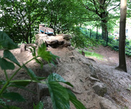 Ein kleiner Spielplatz im Wald mit einem Sandhaufen und Felsen. 