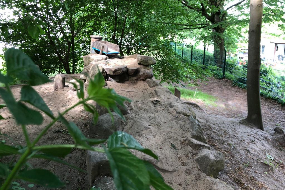 Ein kleiner Spielplatz im Wald mit einem Sandhaufen und Felsen. 
