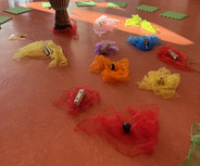 Im Raum liegen mehrere farbige Tücher in Rot, Gelb, Blau, Orange und Lila, die mit verschiedenen Musikinstrumenten wie Klanghölzern und einem Arbeitsplatz aus einem Trommel stehen.