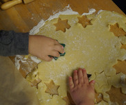 Zwei Kinderhände drücken Ausstechformen in einen flachen Teig auf einer Holzoberfläche. 