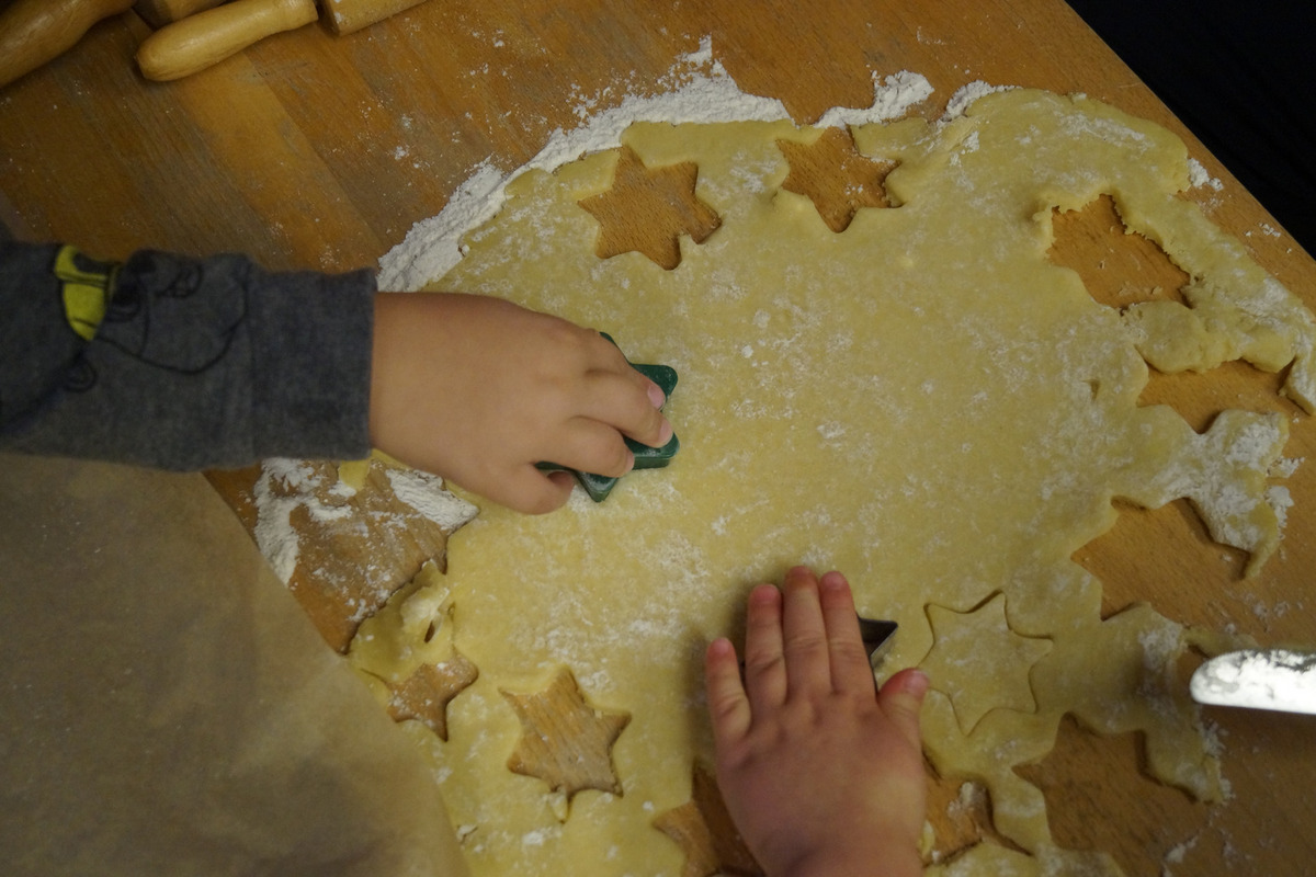 Zwei Kinderhände drücken Ausstechformen in einen flachen Teig auf einer Holzoberfläche. 