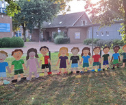 Das Bild zeigt eine Reihe von bunten, aus Pappe ausgeschnittenen Kinderfiguren, die sich an den Händen halten. 