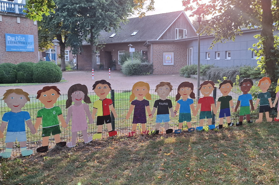 Das Bild zeigt eine Reihe von bunten, aus Pappe ausgeschnittenen Kinderfiguren, die sich an den Händen halten. 