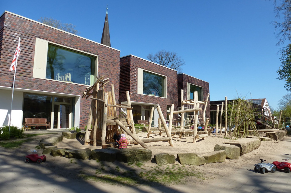 Eine moderne Einrichtung mit einem Spielplatz aus Holz und Sand im Vordergrund. 