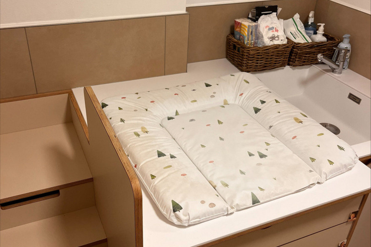 Ein Wickeltisch mit einer abwischbaren Wickelauflage, die mit kleinen Baummotiven bedruckt ist.