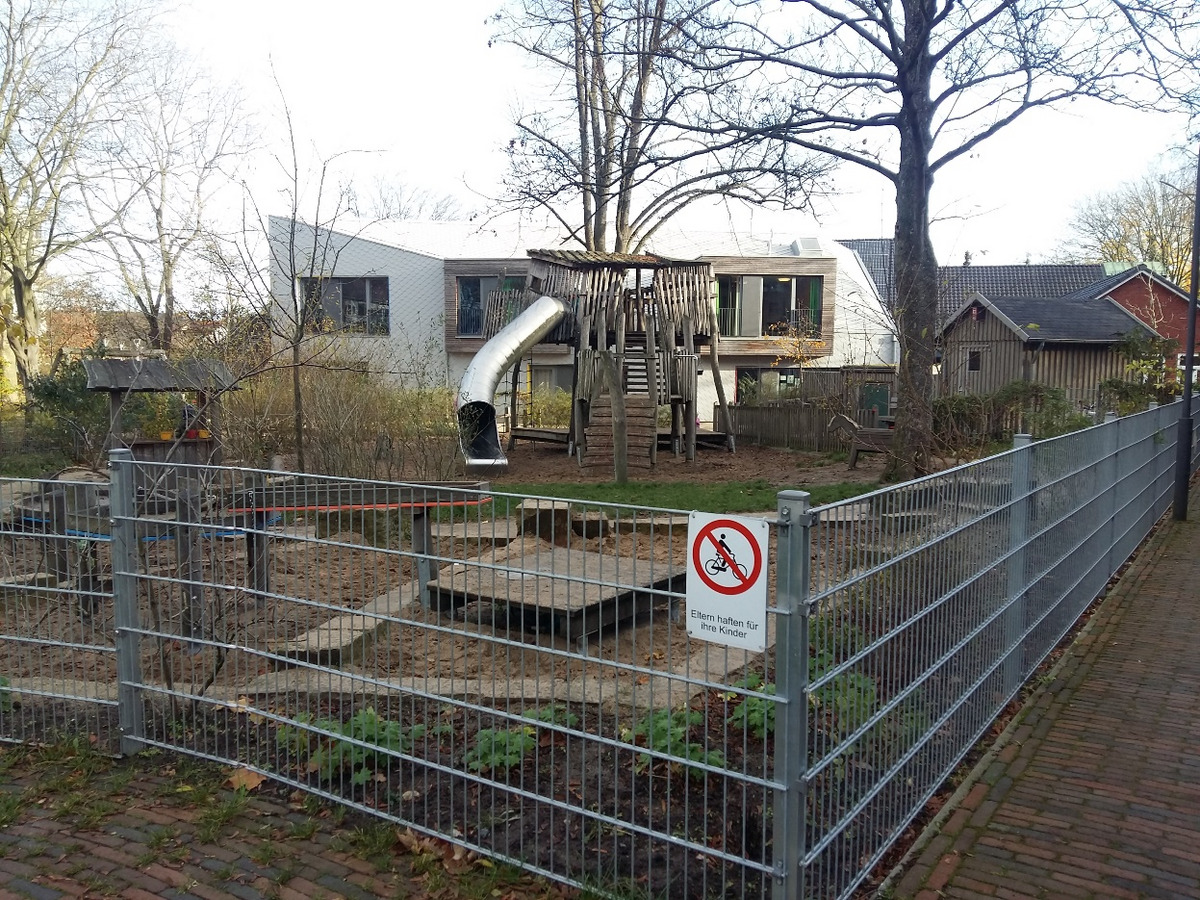Ein Spielplatz mit einer Rutsche und einem Holzspielgerüst steht im Vordergrund.