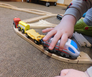 Ein kleines Kind spielt mit einer Holzeisenbahn. Es drückt einen Zug entlang einer kurvigen Schiene. 