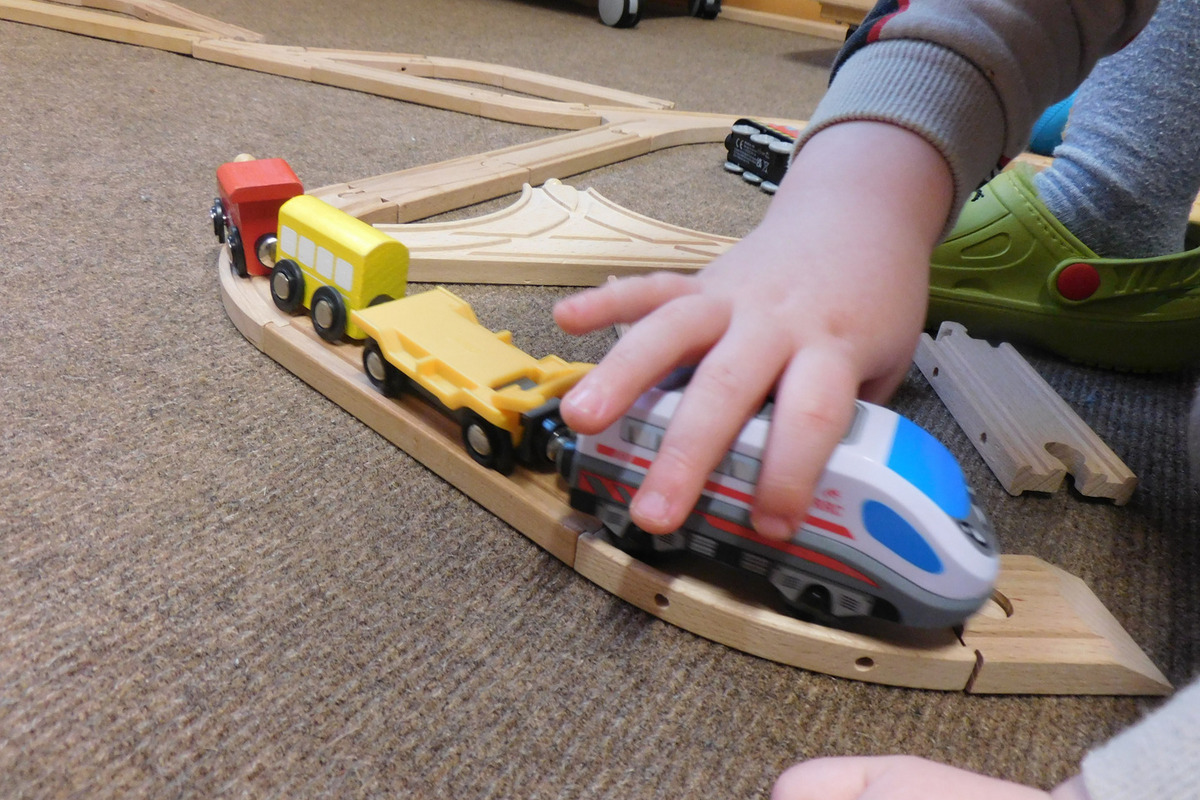 Ein kleines Kind spielt mit einer Holzeisenbahn. Es drückt einen Zug entlang einer kurvigen Schiene. 