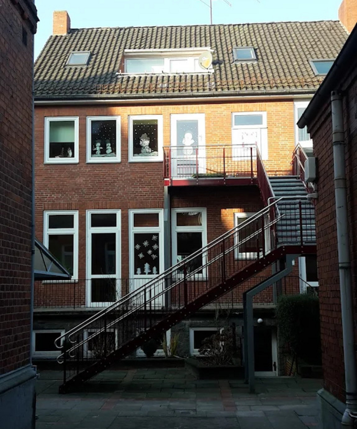 Ein rotes Treppengeländer führt zu einem oberen Eingang eines Backsteinhauses. 