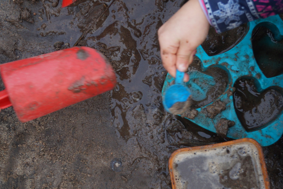 Zwei Hände graben im nassen Sand. 