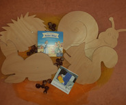 Eine Sammlung von holzgeschnittenen Tieren, darunter ein Igel, ein Hase, ein Eichhörnchen und eine Schnecke, liegt zusammen mit zwei Kinderbüchern. Eines der Bücher ist die „Bilder-Bibel“, das Geschichten von Jesus enthält. 