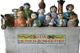 Eine Skulpturengruppe aus farbenfrohen Figuren von Kindern, Tieren und einer Pferdestatue, die auf einem grauen Sockel stehen. Am Sockel steht der Schriftzug „Kita Dietrich-Bonhoeffer“.