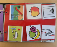 Das Bild zeigt ein buntes Arbeitsheft mit mehreren Symbolen. Darunter sind Bilder von einer Rutsche, einer Frucht, einer Waschaktion und Händen, die sich berühren. Die Symbole können zur Kommunikation oder als Lernhilfen verwendet werden.