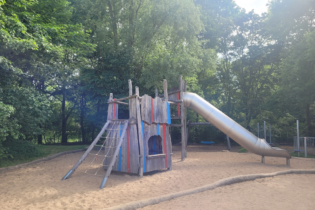 Ein Spielplatz mit einem bunten Klettergerüst aus Holz und einer silbernen Rutsche. 
