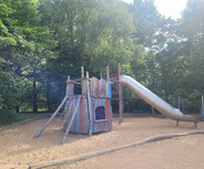 Ein Spielplatz mit einem bunten Klettergerüst aus Holz und einer silbernen Rutsche. 