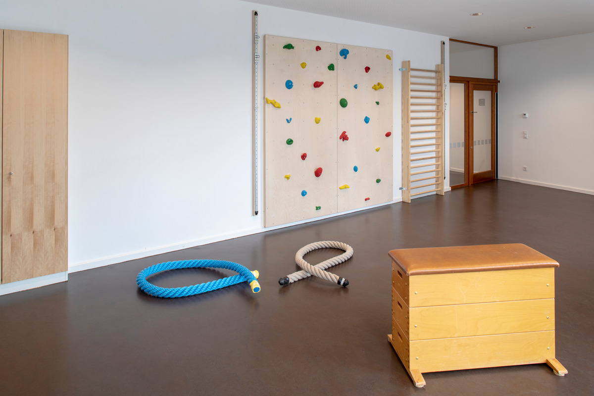 Ein heller Raum mit einer Kletterwand, die mit bunten Griffen ausgestattet ist.