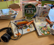 Auf einem Tisch liegen mehrere Kinderbücher und tiptoi-Stifte. Die Bücher umfassen Themen wie Musik, Feuerwehr und Tiere. Neben den Büchern befindet sich ein Paar Kopfhörer, die für die Interaktivität mit den tiptoi-Büchern verwendet werden.
