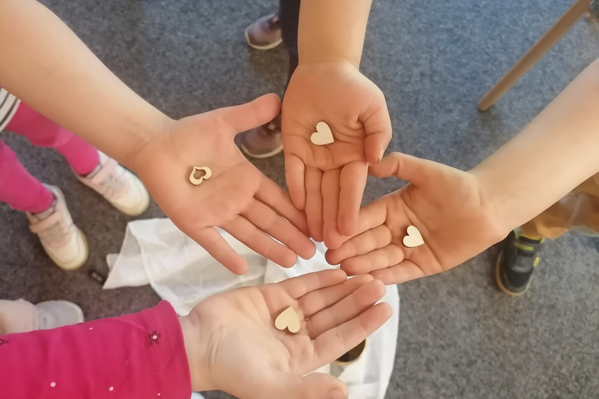 Vier Hände von Kindern halten kleine, herzförmige Holzstücke. Die Hände sind offen und zeigen die Herzen.