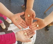 Vier Hände von Kindern halten kleine, herzförmige Holzstücke. Die Hände sind offen und zeigen die Herzen.