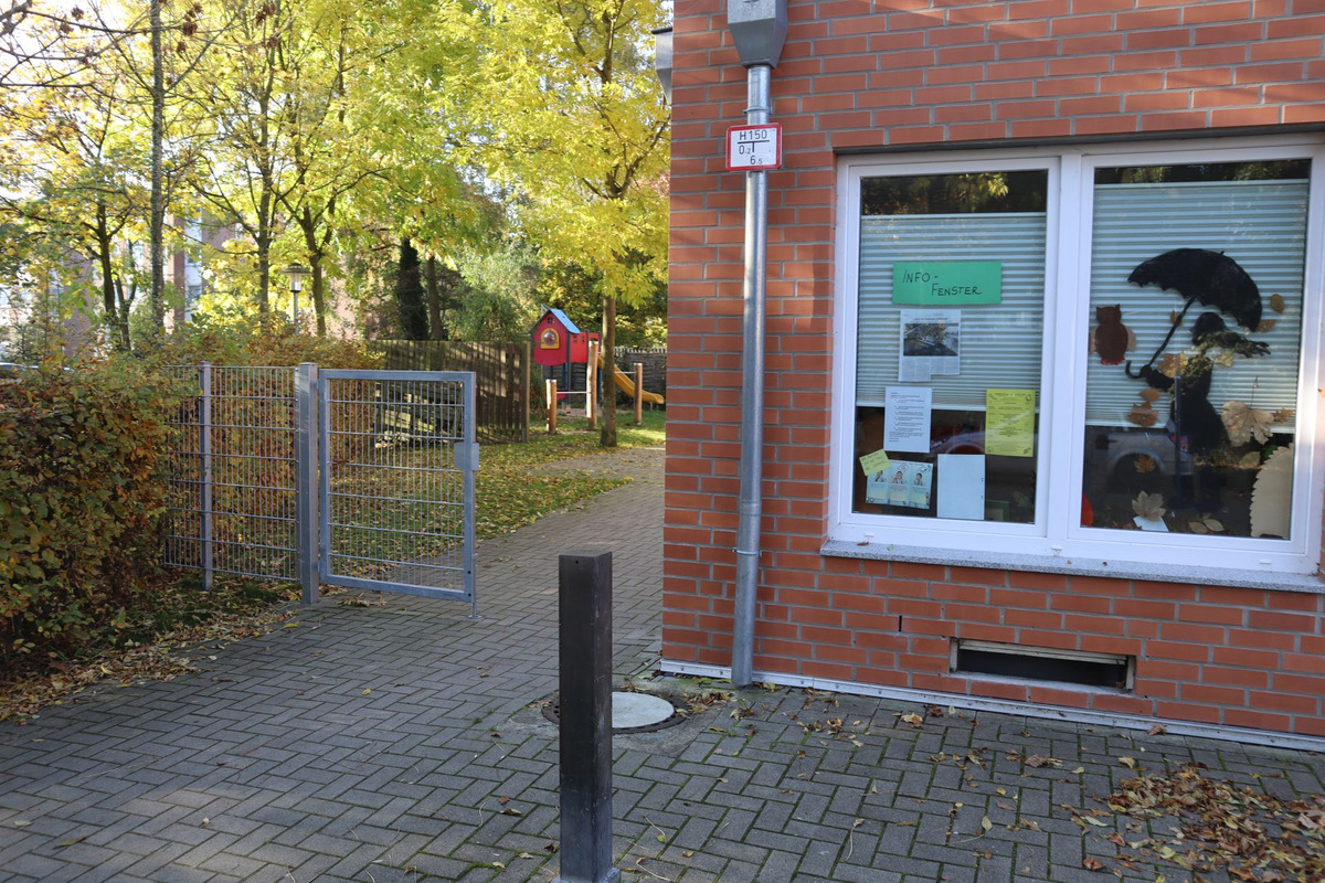 Eingang zu einem Spielplatz mit einem offenen Tor, das zu einem gepflasterten Weg führt.