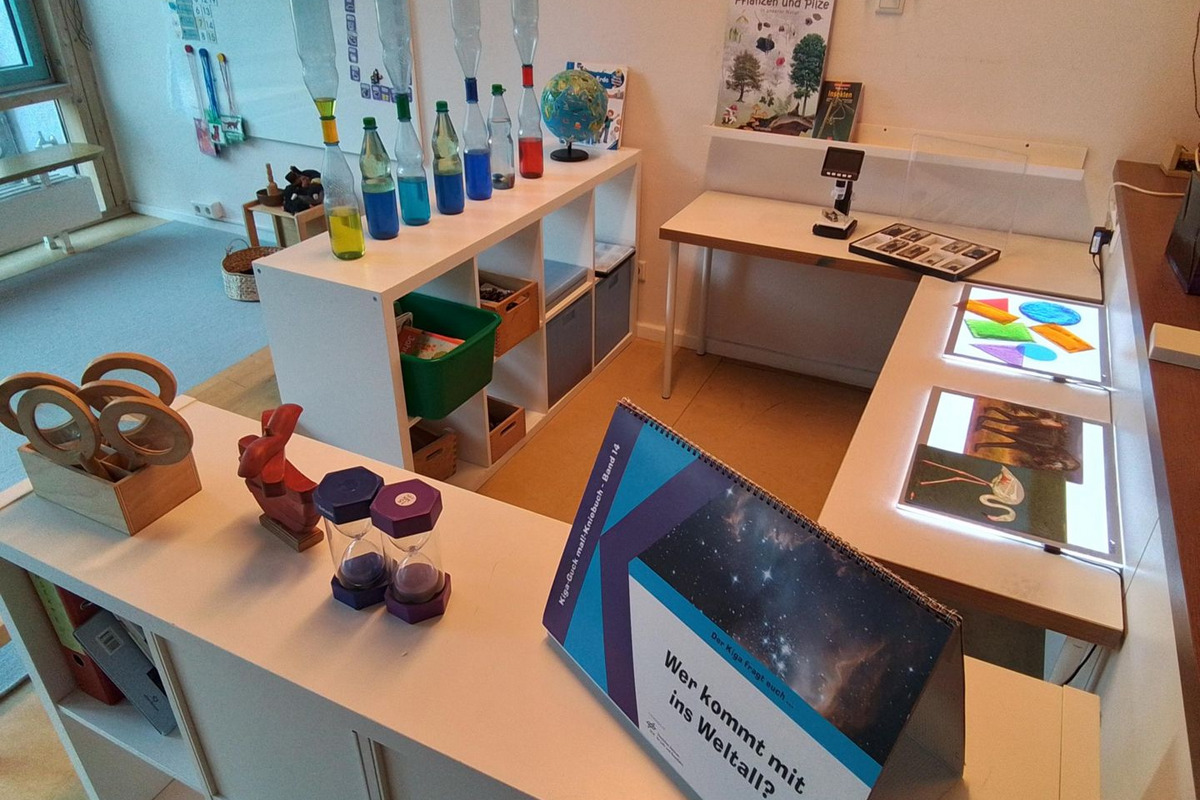 Ein heller Raum mit verschiedenen Tischen, auf denen wissenschaftliche Materialien und Experimente präsentiert werden. 