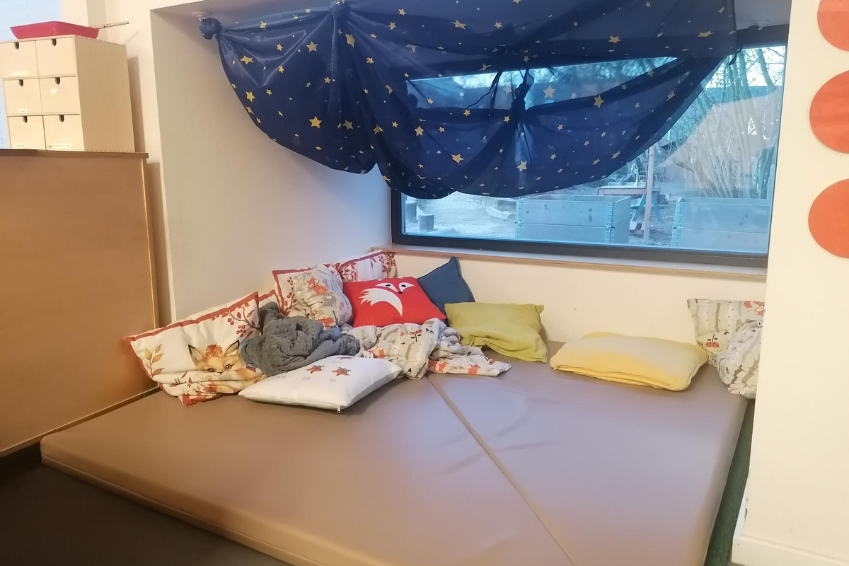 Ein gemütlicher, gepolsterter Bereich mit verschiedenen Kissen liegt unter einem Fenster. 